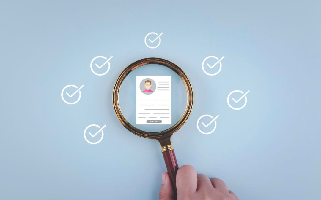 A hand holds a magnifying glass over a resume, surrounded by checkmarks on a blue background.