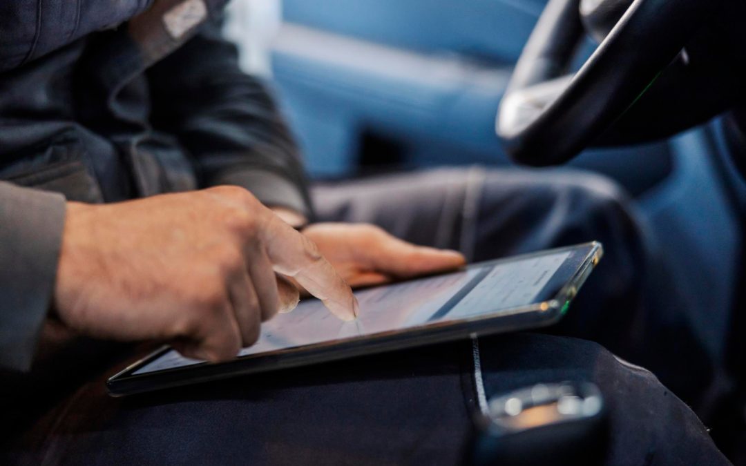 A person uses a tablet while sitting in a car, with one finger touching the screen.