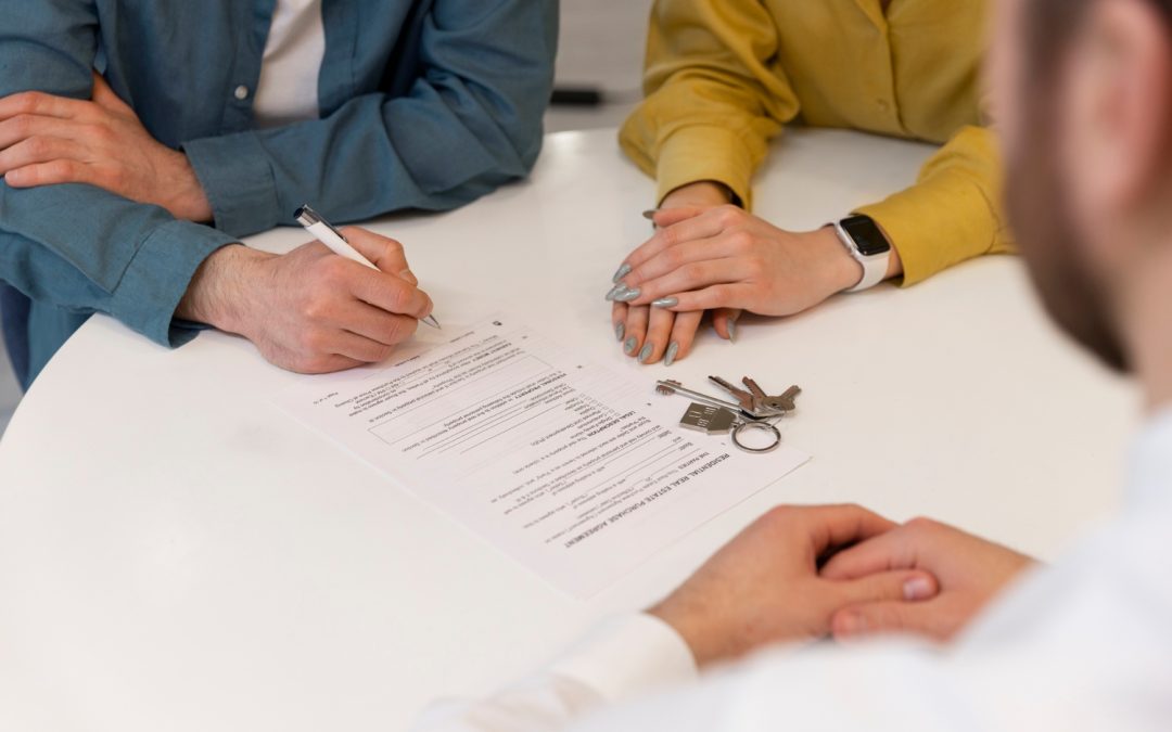 Three people at a table sign paperwork with keys on the table, possibly finalizing a real estate deal.