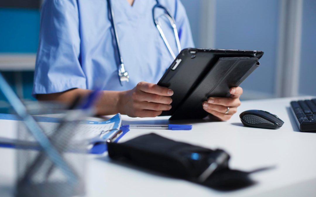 A medical professional in blue scrubs using a tablet at a desk.